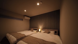 Una habitación de hotel con dos camas, una mesita de noche con lámpara y cabecero de madera.
