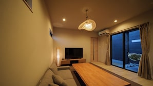 Una sala de estar moderna con una mesa de centro de madera, un sofá, un televisor de pantalla plana y un ventanal con cortinas.