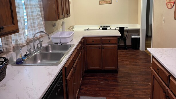 A kitchen with wooden cabinets, a marble countertop, a sink, and a trash can.