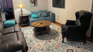 A living room with a brown leather sofa, a blue couch, a black leather armchair, a wooden coffee table, and a patterned rug.