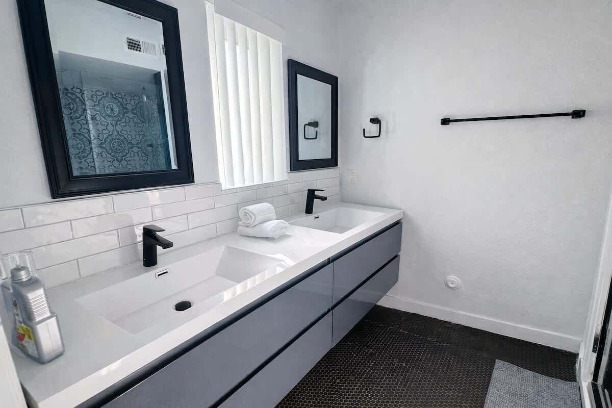 Un baño moderno con un lavamanos blanco, un grifo negro y dos espejos.