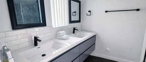 Un baño moderno con un lavamanos blanco, un grifo negro y dos espejos.