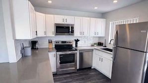 Una cocina moderna con armarios blancos, electrodomésticos de acero inoxidable y piso de madera oscura.