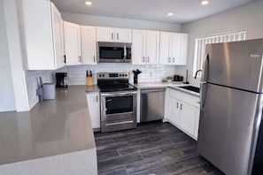 A modern kitchen with white cabinets, stainless steel appliances, and a dark wood floor. - Iris - In Old Town-Walk to Best Spots in Old Town (Scottsdale)