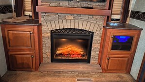 A fireplace with a stone surround, a TV above it, and wooden cabinets on either side. - The Premier Cuero Tx RV ,No Cleaning Fee,King Bed, Sectional Couch (Cuero)