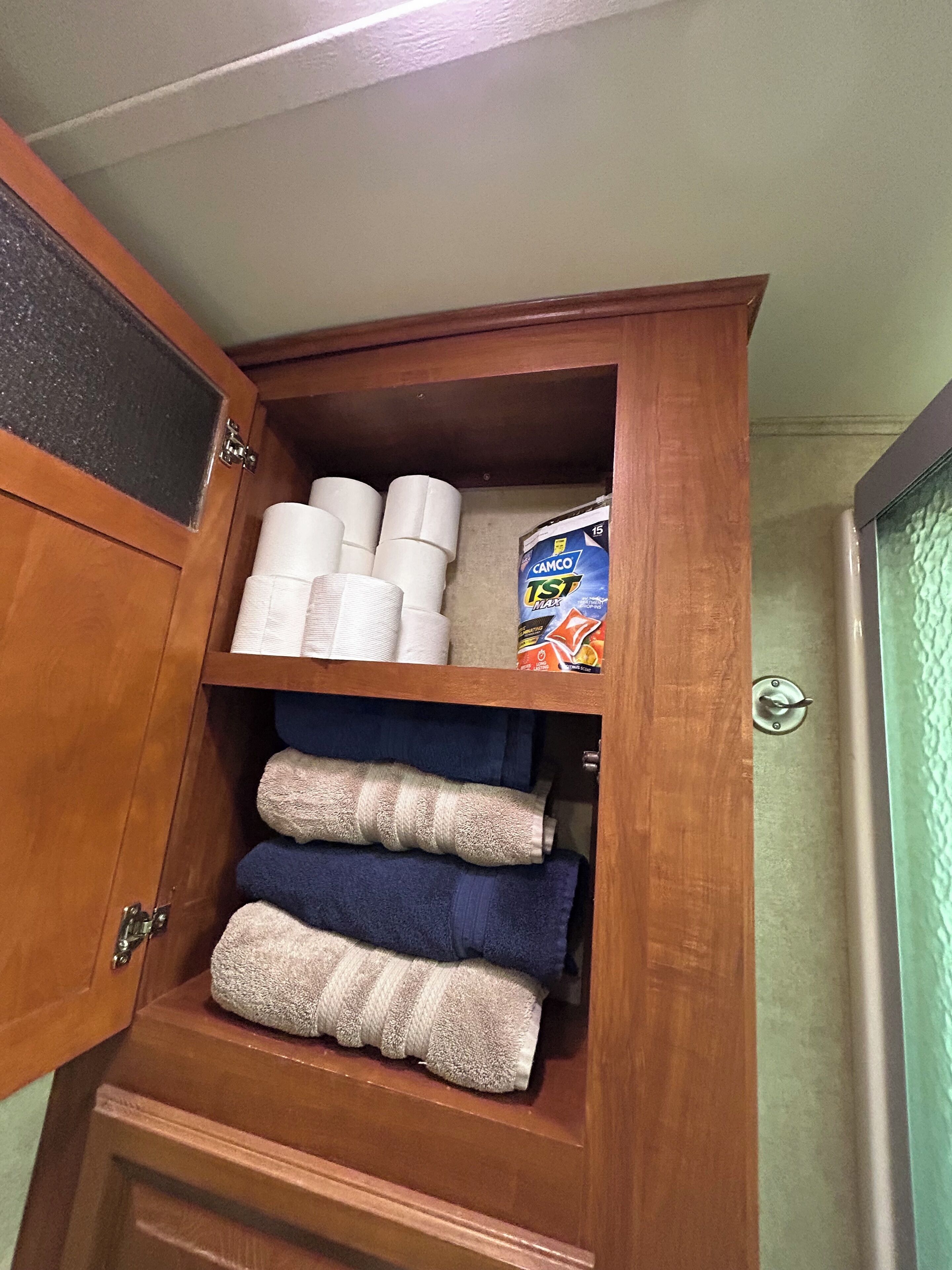 A wooden cabinet with towels and a box of Camco 1st Max tissue.