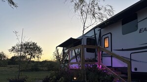 A stationary RV with a covered porch area, surrounded by potted plants and a stone pathway. - The Premier Cuero Tx RV ,No Cleaning Fee,King Bed, Sectional Couch (Cuero)