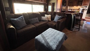 A cozy RV interior with a brown leather couch, a small ottoman, and wooden cabinets. - The Premier Cuero Tx RV ,No Cleaning Fee,King Bed, Sectional Couch (Cuero)