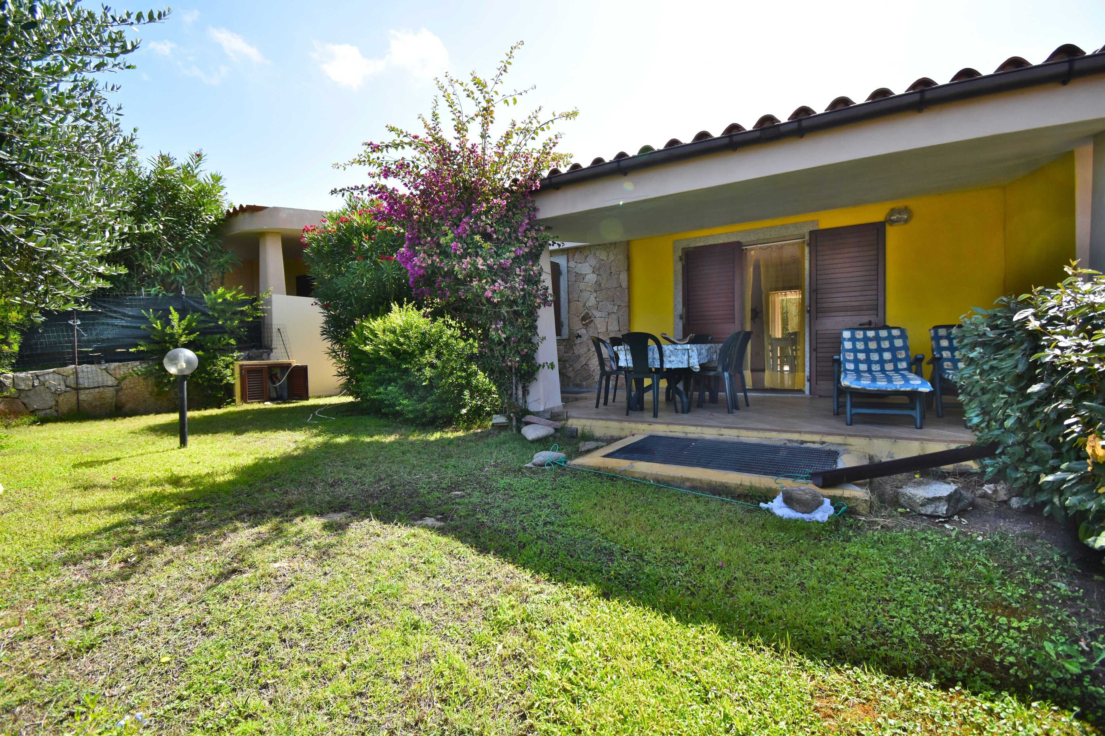 A house with a yellow exterior, a covered patio with outdoor furniture, and a well-maintained garden.
