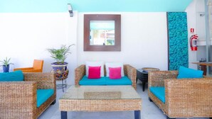A sunlit outdoor seating area with wicker furniture and teal cushions, a small table, and a fire extinguisher on the wall. - Modern Downtown Retreat | Comfortable and Convenient Stay in Cancun (Cancún)
