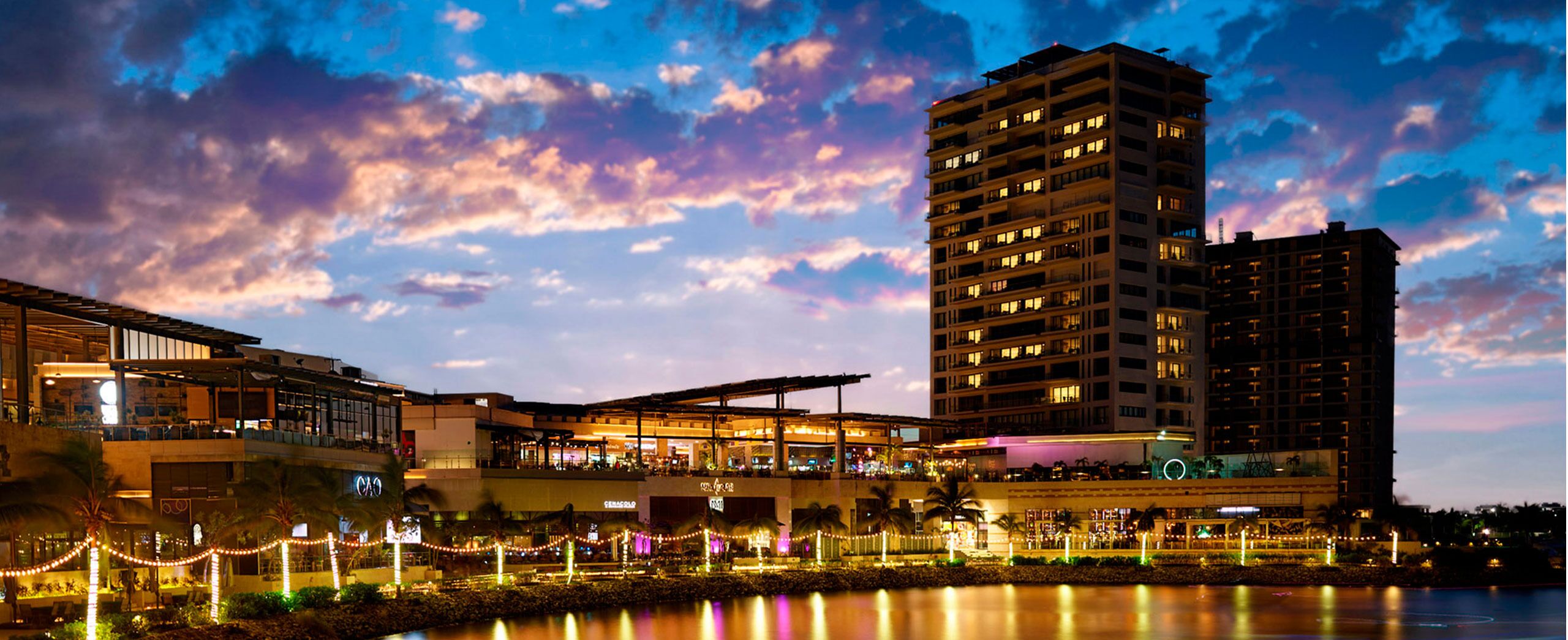 A hotel with multiple floors, a waterfront view, and outdoor seating areas with string lights.