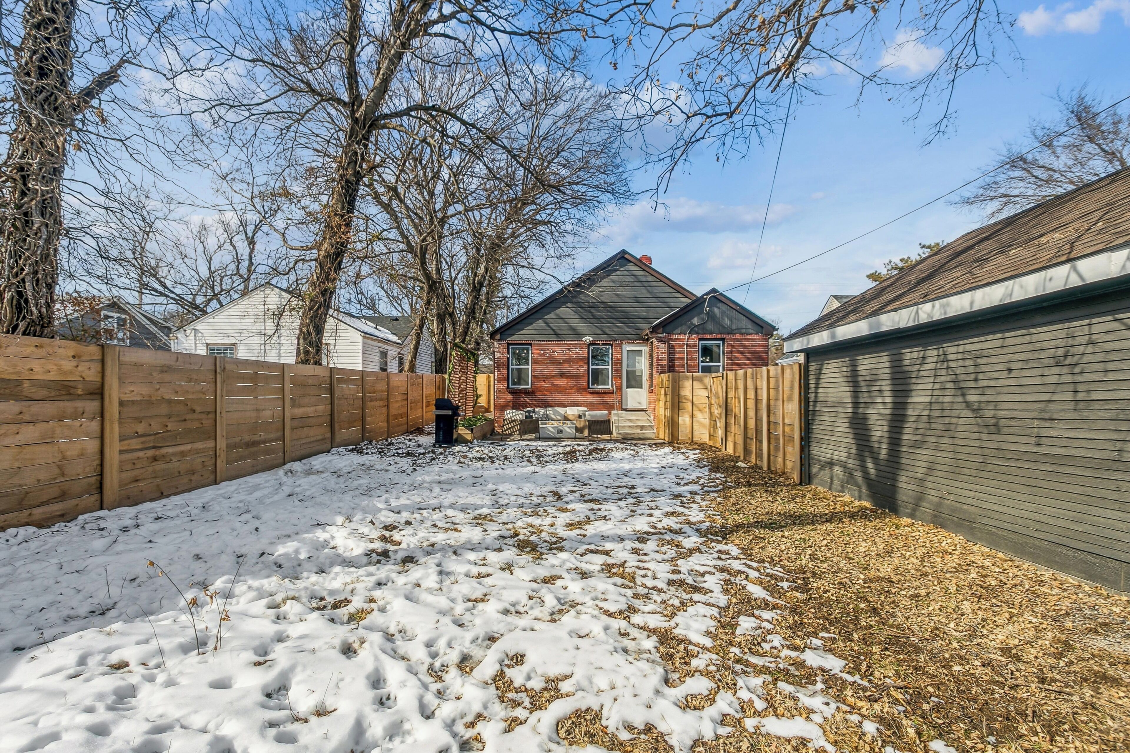 Un jardin avec une clôture en bois, une maison en briques et un garage.