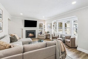A modern living room with a fireplace, comfortable seating, and a view of the outdoors through large windows.