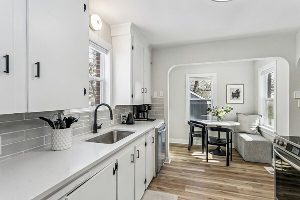 A modern kitchen with white cabinetry, a double sink, and a dining area with a table and chairs.