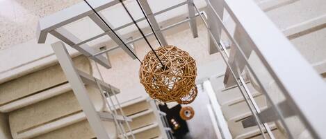A modern interior with a hanging spherical wicker light fixture, white railings, and a reflective floor.