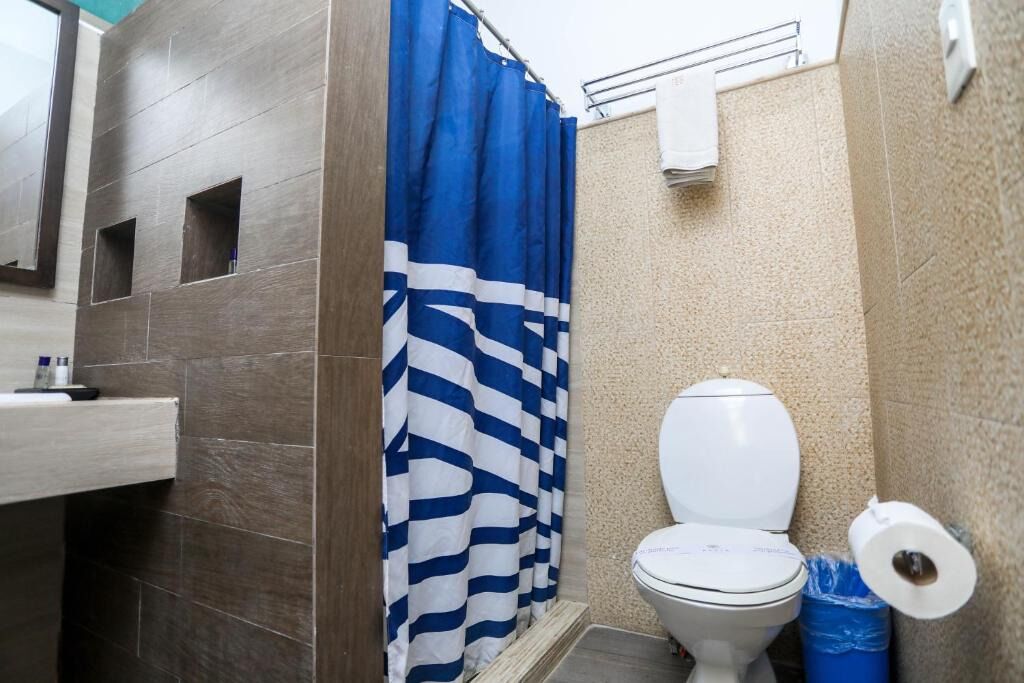 A bathroom with a shower curtain, a toilet, and a trash bin.