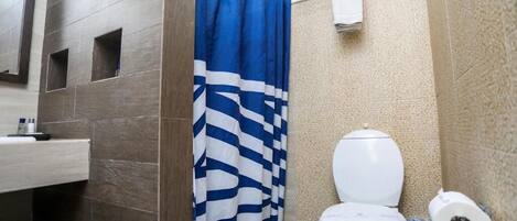 A bathroom with a shower curtain, a toilet, and a trash bin.