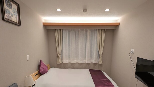 Une chambre à coucher avec un lit, un canapé gris, un téléviseur et un tapis de course.