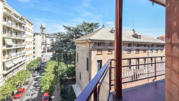 A balcony with a view of a street lined with trees and buildings, including a church with a clock tower. - Cozy apartment in Savona with WiFi (Savona)