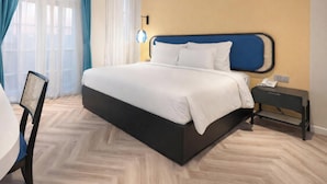 A hotel room with a large bed, a bedside table with a phone, and a chair. - HAN Sunset Milan Hotel & Spa (Phu Quoc)