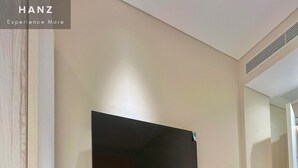 A modern room with a flat-screen TV mounted on the wall, a desk with a chair, a small heater, and a trash bin. - HAN Sunset Milan Hotel & Spa (Phu Quoc)