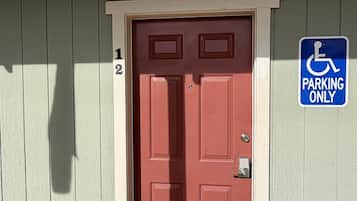A red door with a handicap parking sign, a doormat with palm trees, and a light fixture above the door.