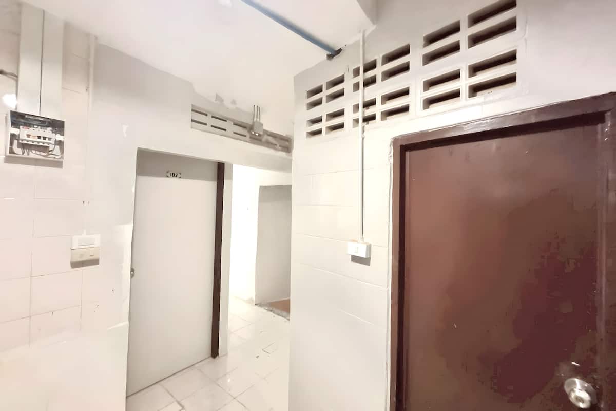 Un pasillo con paredes de azulejos blancos, una puerta de marco marrón y una rejilla de ventilación en la pared.