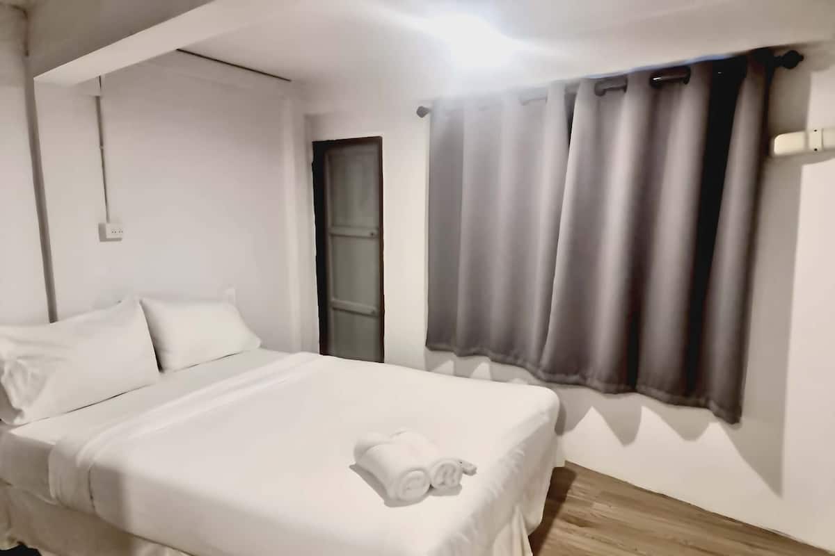 Una habitación de hotel con cama, ventana con cortinas y suelo de madera.