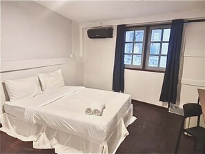 A neatly made bed with white linens, a single pillow, and two decorative pillows. There is a window with curtains, a chair, and a wall-mounted air conditioning unit. - Znap Yaowarat (Bangkok)