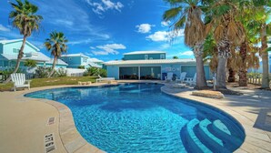Una piscina con agua azul cristalina, rodeada de palmeras y un edificio con techo blanco.