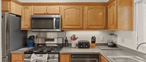 A modern kitchen with wooden cabinets, stainless steel appliances, a microwave, a gas stove, a dishwasher, and a sink.
