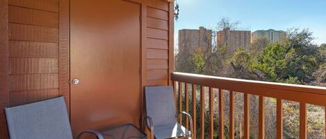 A balcony with two chairs, a wooden door, and a view of buildings and trees.