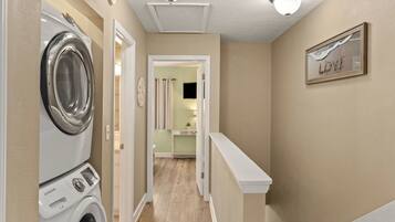 A laundry room with a front-loading washer and dryer, a hallway leading to a bathroom, and a 'LOVE' sign on the wall.