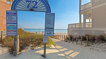 A beach entrance with a sign indicating beach rules and a no lifeguard warning.