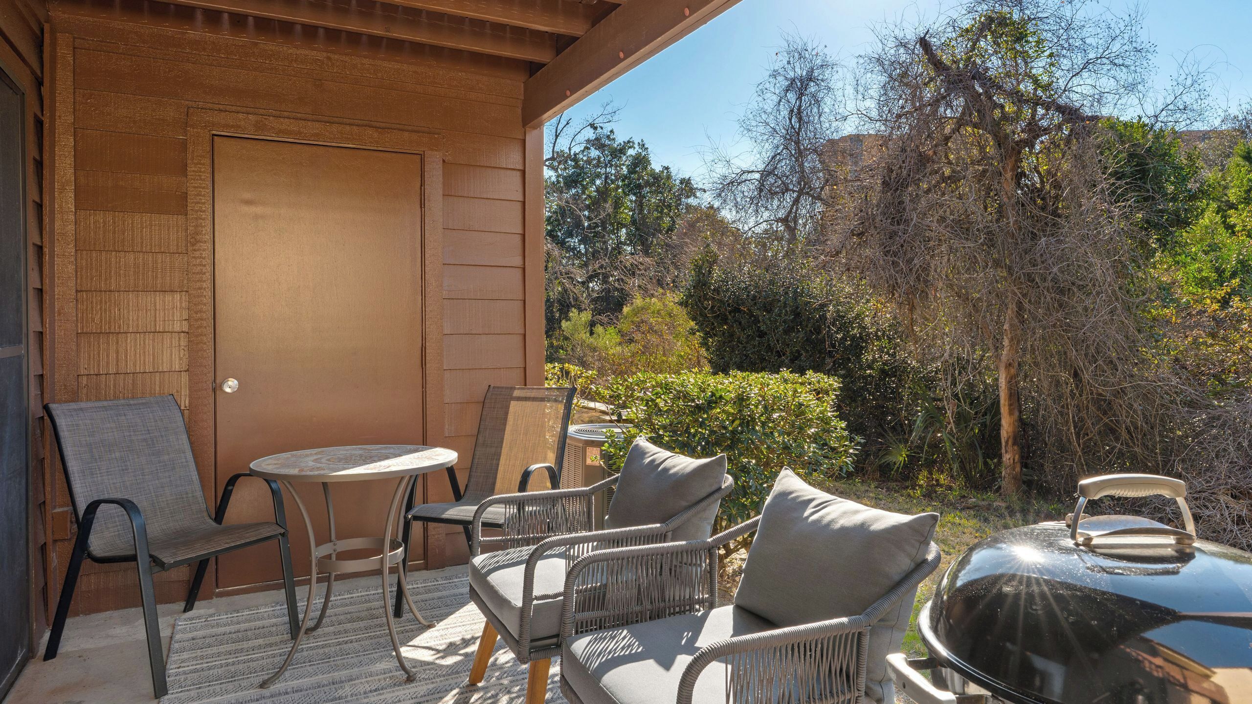 A covered patio with wicker furniture, a table, and a grill.