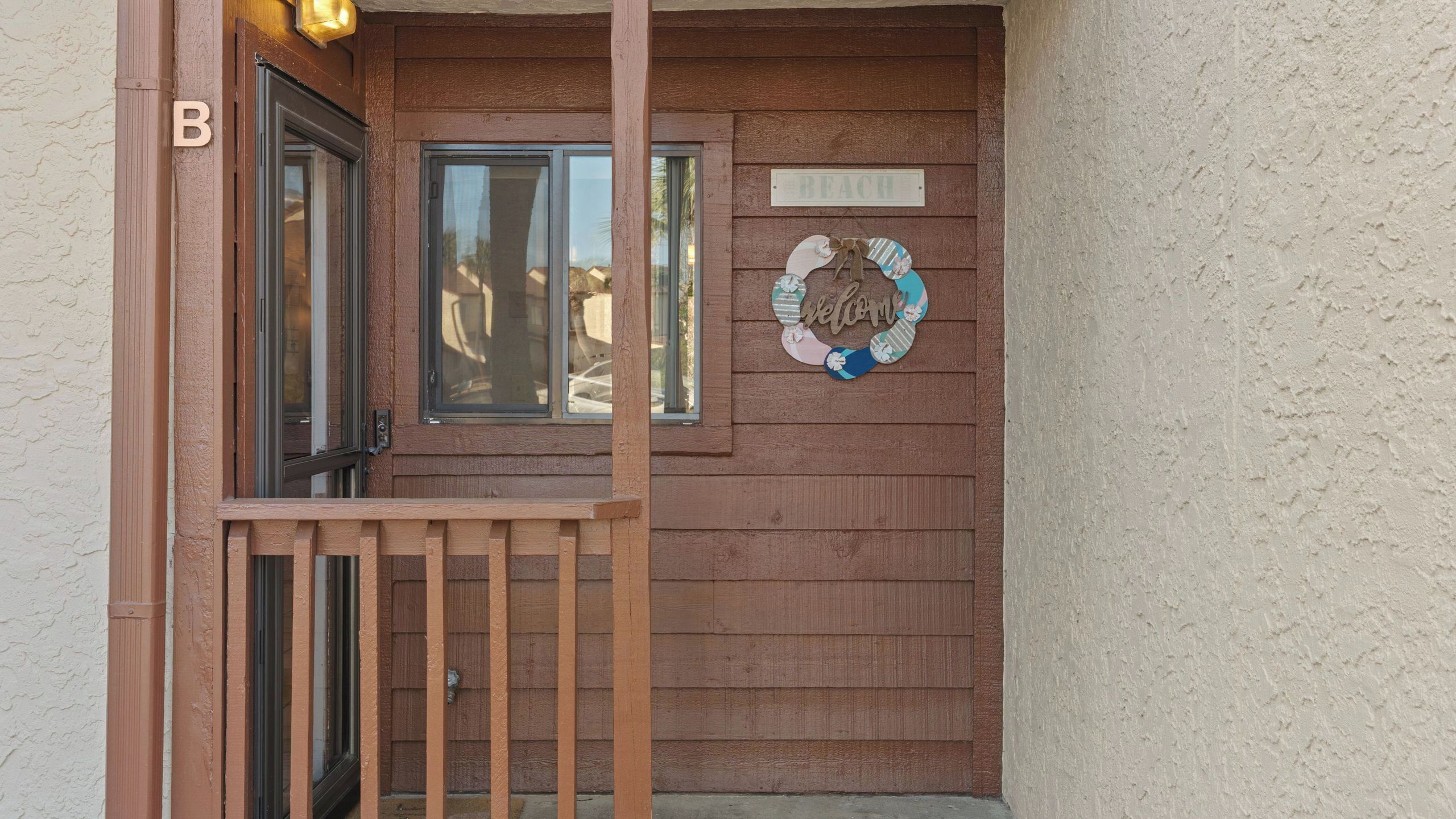 A wooden door with a 'Welcome' sign, a mailbox, and a 'B' sign on the wall.
