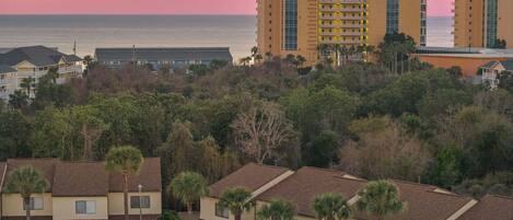 A residential area with multiple-story buildings, some with balconies, and a view of the ocean at sunset.