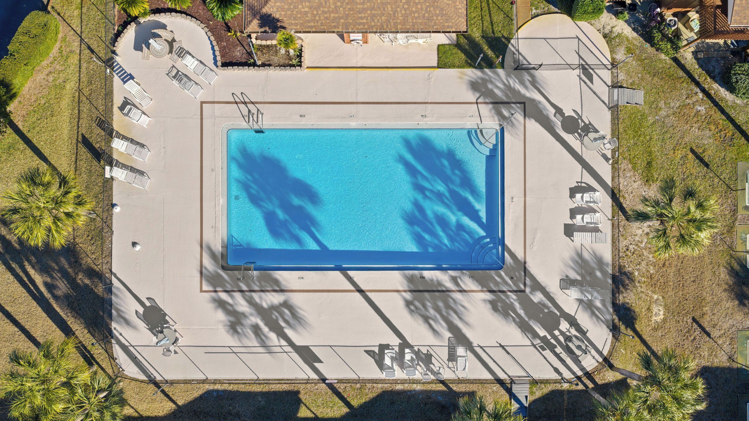 An aerial view of a swimming pool with surrounding lounge chairs and a covered area.
