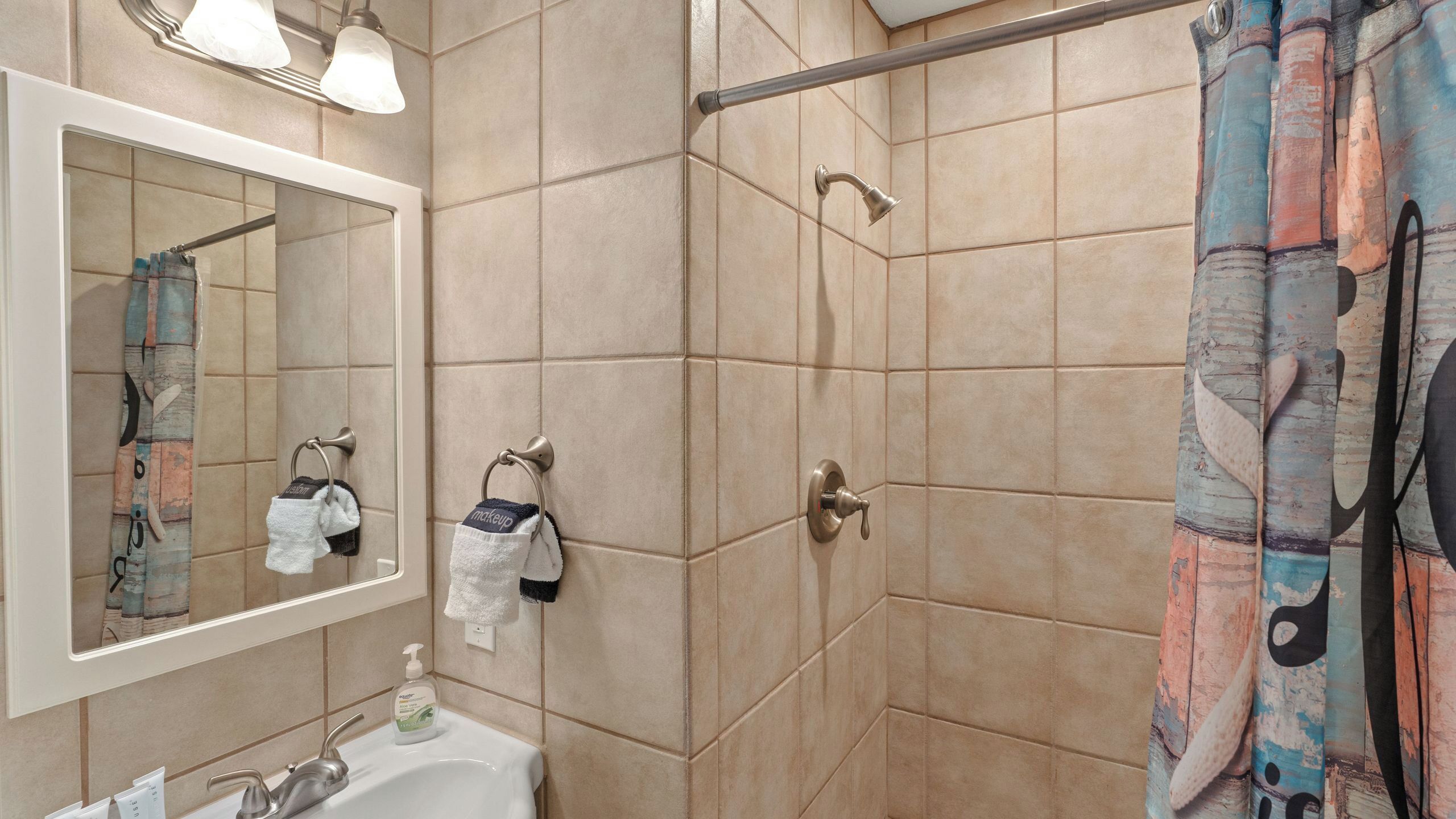 A bathroom with a sink, mirror, towel rack, shower curtain, and tiled walls.