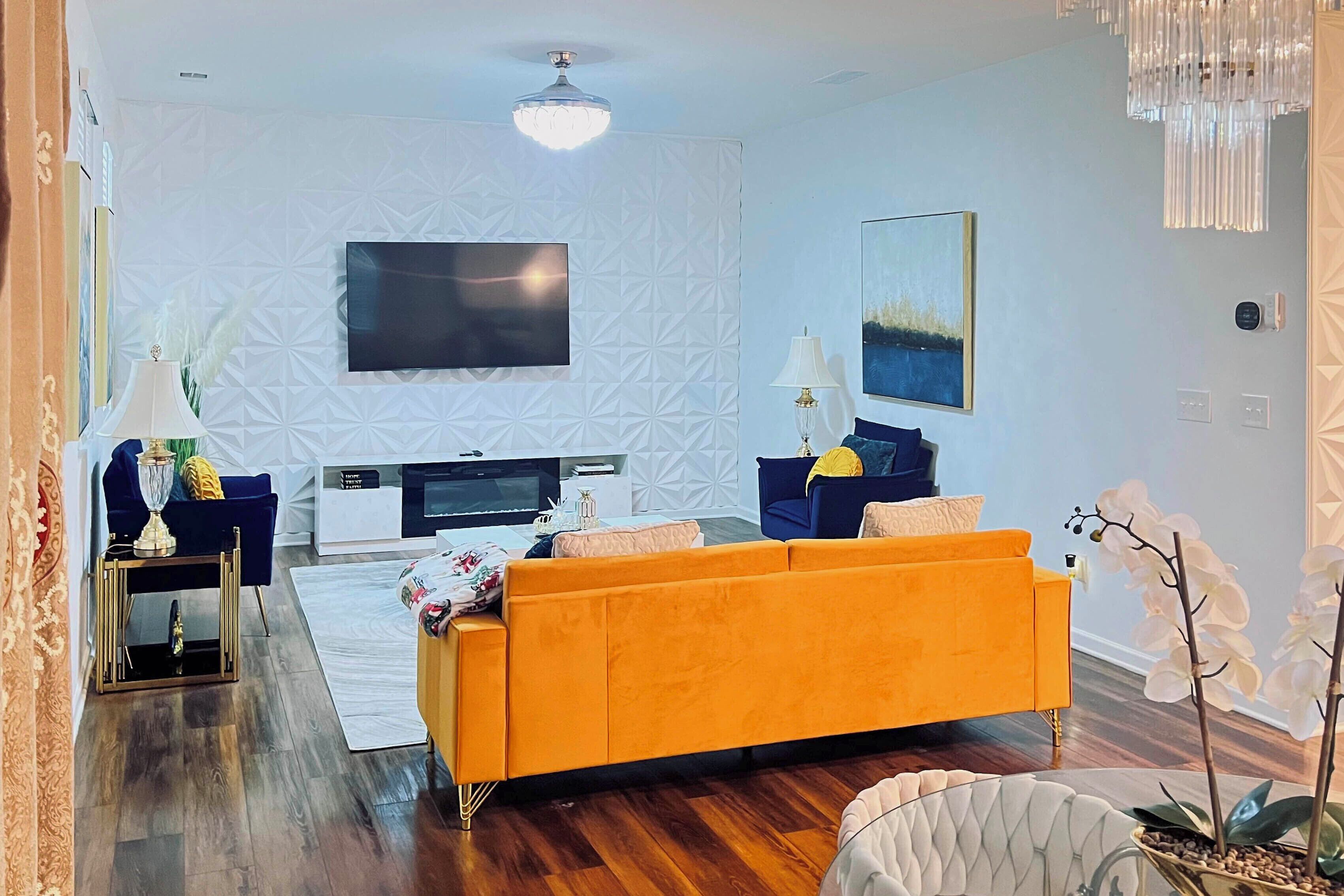 Una sala de estar moderna con un televisor de pantalla plana grande, un sofá amarillo y una pared de acento blanca.