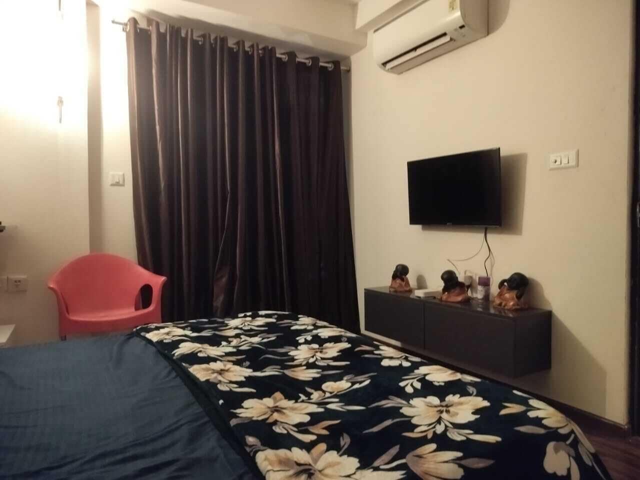 Ein Hotelzimmer mit einem Bett, einem roten Sessel, einem Flachbildfernseher und einer Kommode mit Dekoration.