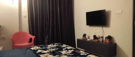 Ein Hotelzimmer mit einem Bett, einem roten Sessel, einem Flachbildfernseher und einer Kommode mit Dekoration.