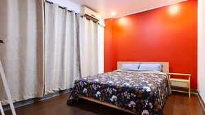 Een slaapkamer met een bed, gordijnen, een houten vloer en een rode wand.