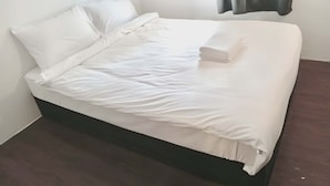 Een netjes opgemaakt bed met wit beddengoed, een donker houten hoofdbord en een raam met donkere gordijnen.
