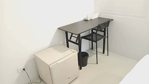Een kleine, witte kitchenette met een koelkast, een zwarte prullenbak en een tafel met stoelen.