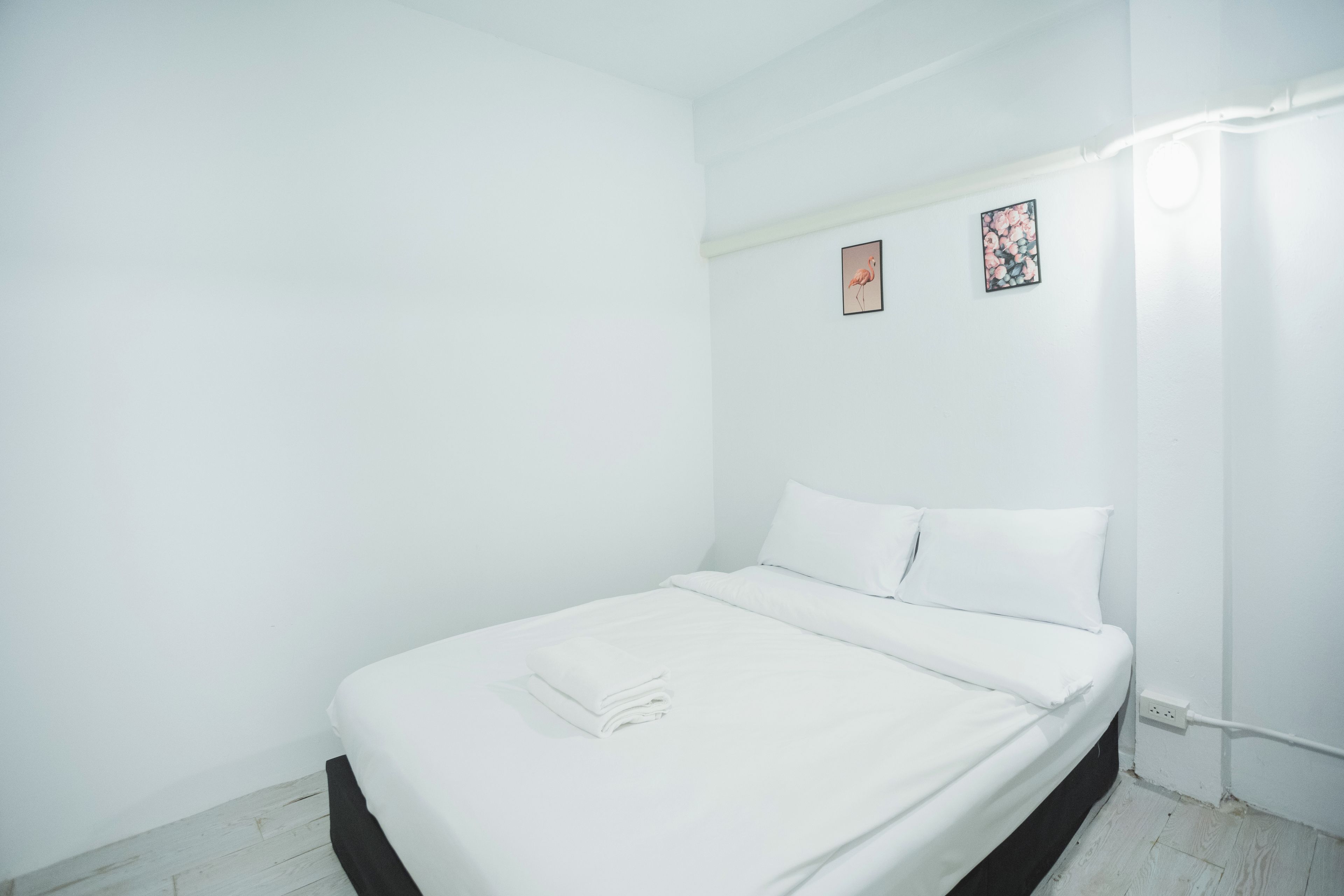 Una habitación blanca con una cama, una lámpara de pared y dos cuadros pequeños.