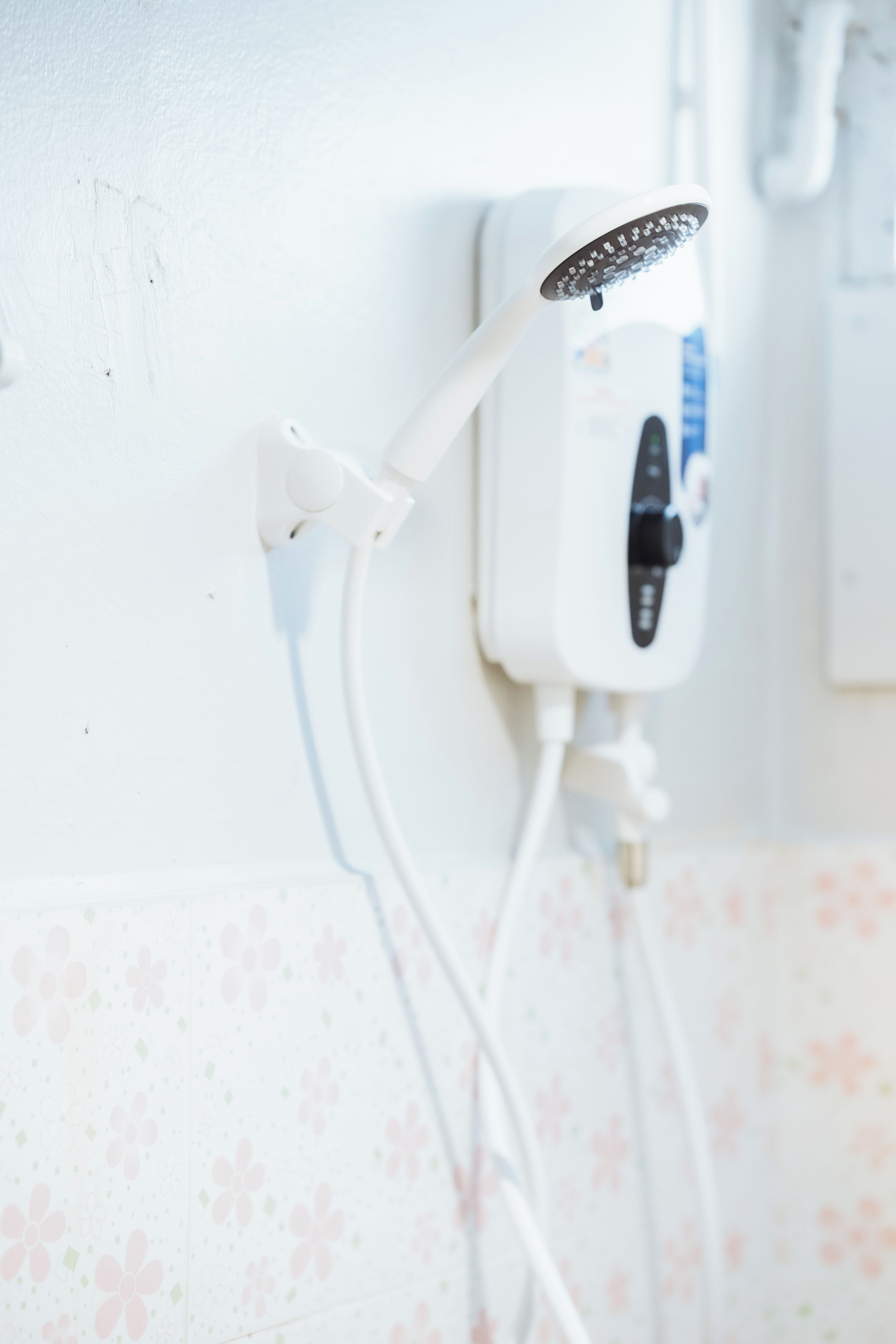 A shower with a handheld showerhead mounted on a wall, connected to a power outlet.