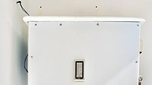 Een witte, vierkante wandunit met metalen frame, een ingebouwd keypad en een klein raampje.