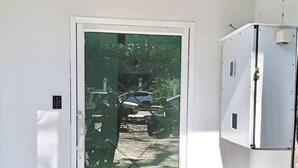 Een deur met een matglazen ruit, een witte muur en een klein wit kastje aan de rechterkant.