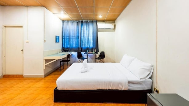 Une chambre d’hôtel avec un lit, un bureau, deux chaises, une petite table et une fenêtre avec des rideaux.
